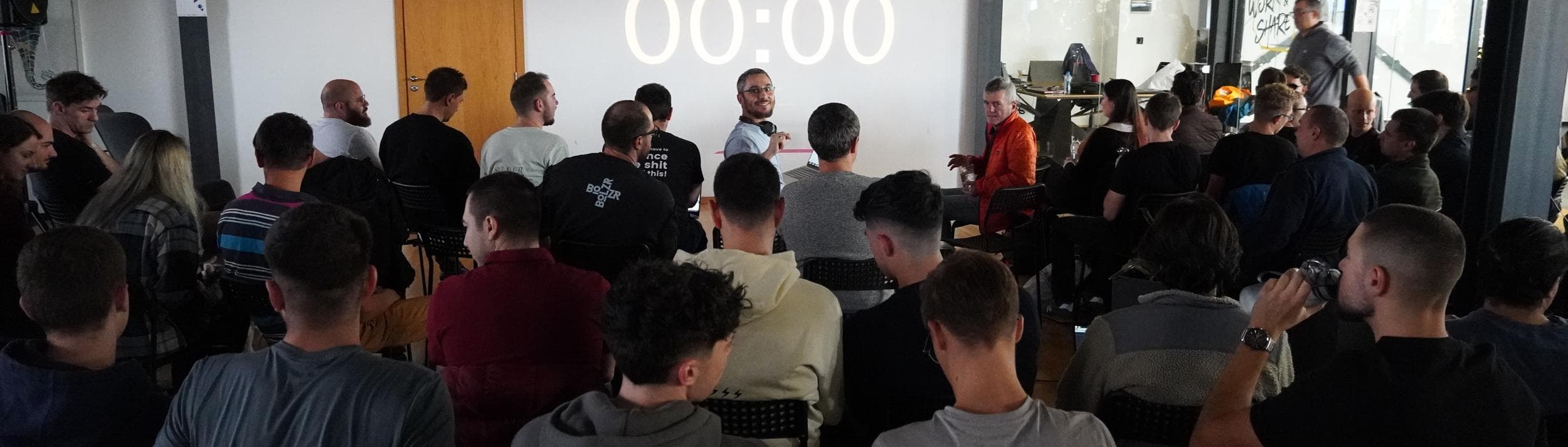 A full room at an AIE.F Europe meetup, watching a speaker present in front of a countdown timer.